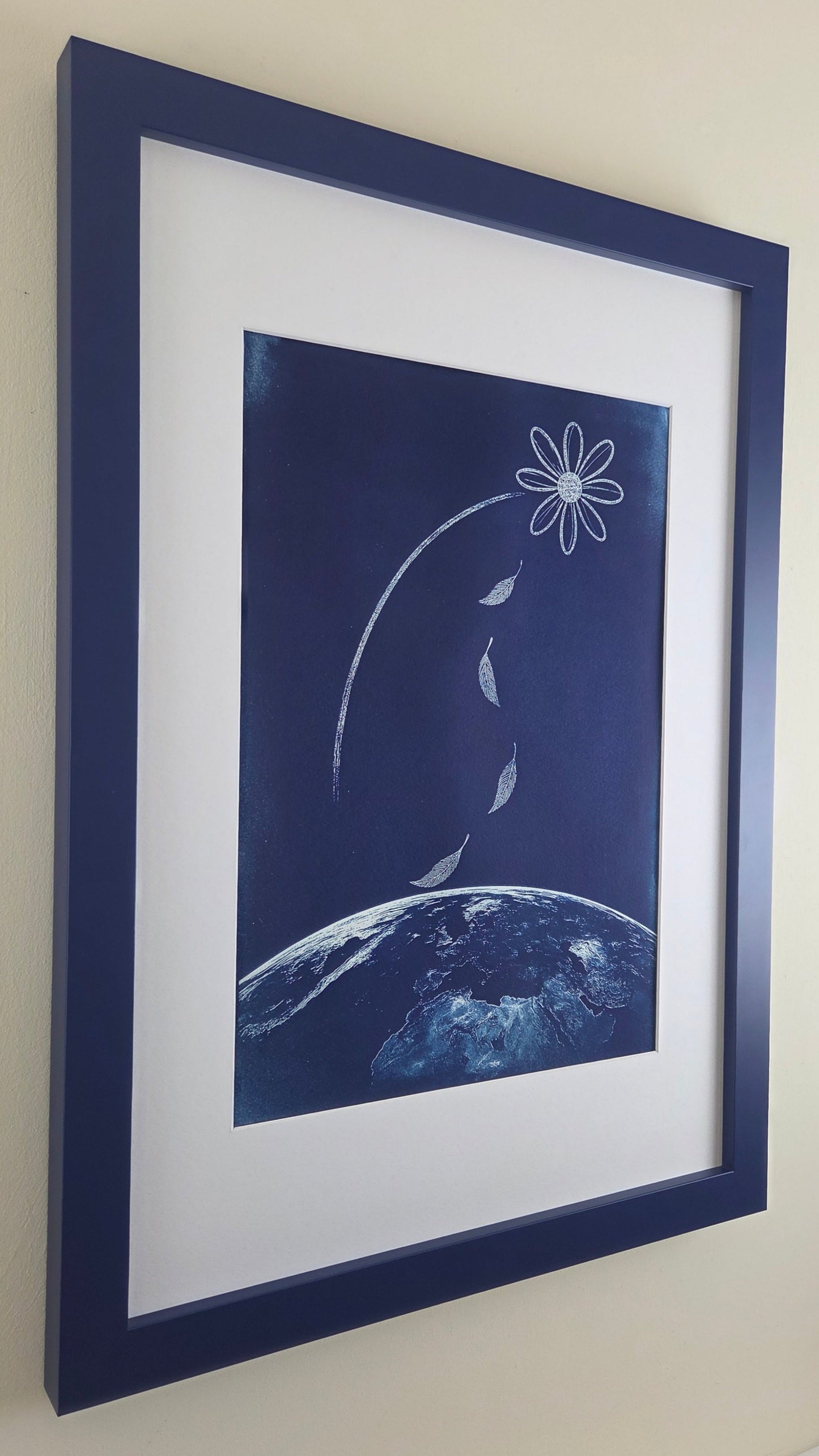 Framed artwork of a stylized flower and planet on a beige wall